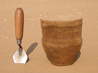 a neolithic pot next to a trowel