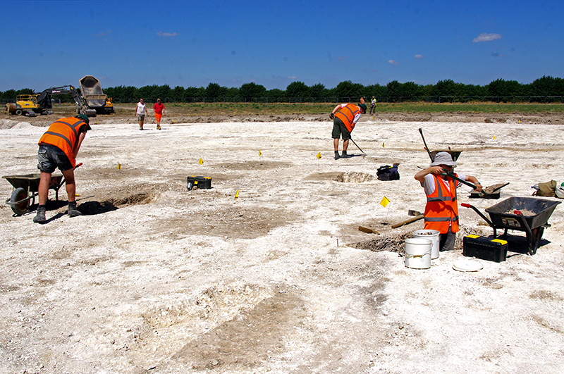 people excavating in a field and digger in background