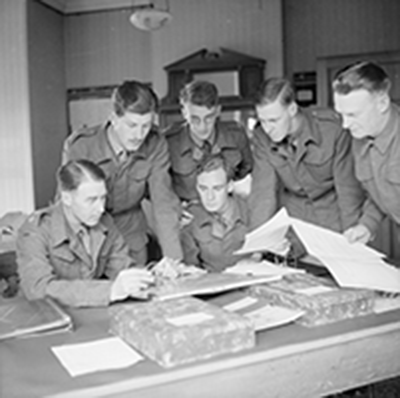wartime photo of six officers gathered around a desk reviewing paperwork